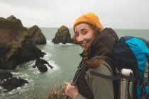 Ritratto di donna escursionista sorridente in piedi sulla costa del mare e guardando la macchina fotografica — Foto stock