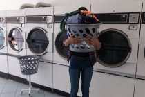 Woman carrying laundry basket at laundromat — Stock Photo