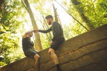 Hombre en forma ayudando a su compañero de equipo a escalar una pared de madera en el campamento de entrenamiento - foto de stock