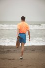 Vue arrière de l'homme s'étirant sur le rivage à la plage — Photo de stock