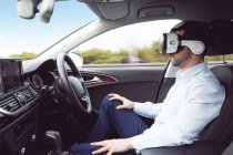 Empresário usando headset realidade virtual em um carro moderno — Fotografia de Stock