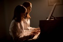 Братья и сестры вместе играют на фортепиано в музыкальной школе — стоковое фото