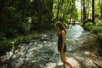 Schöne Frau bewegt sich in Richtung Flussküste im grünen Wald — Stockfoto