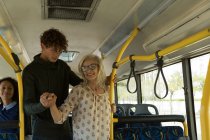 Молодой человек помогает пожилой женщине во время поездки в автобусе — стоковое фото