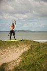 Surfista con tavola da surf che fa esercizio di stretching in spiaggia in una giornata di sole — Foto stock