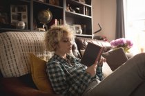 Молода жінка читає книгу у вітальні вдома — стокове фото