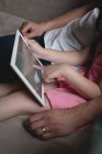 Sección media del padre y la hija usando tableta digital en la sala de estar en casa - foto de stock