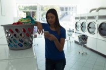 Jeune femme utilisant le téléphone à laverie automatique — Photo de stock