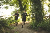 Dos hombres corriendo juntos en el campamento de entrenamiento en un día soleado - foto de stock
