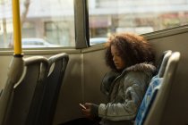 Adolescente usando el teléfono móvil mientras viaja en el autobús - foto de stock