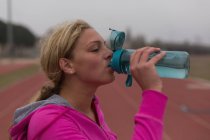 Female athlete drinking water at running track — Stock Photo
