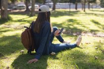 Jovem mulher sentada no parque usando telefone celular — Fotografia de Stock