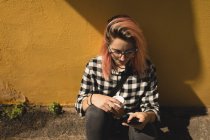 Молодая женщина с помощью мобильного телефона сидит на тротуаре — стоковое фото