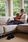 Мати і дитина сидять на дивані і використовують цифровий планшет вдома — стокове фото