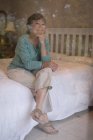 Задумчивая пожилая женщина сидит дома на кровати — стоковое фото