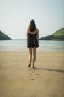 Vue arrière de la femme marchant sur la plage par une journée ensoleillée — Photo de stock