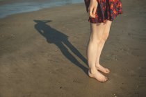 Baixa seção de mulher brincando com sua sombra na praia — Fotografia de Stock