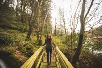 Рыжеволосая женщина-туристка ходит по мосту в лесу — стоковое фото