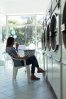 Femme réfléchie prenant un café en attendant à la laverie automatique — Photo de stock