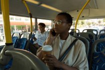 Mulher falando no celular enquanto toma café no ônibus — Fotografia de Stock