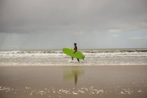 Vista lateral del surfista con tabla de surf caminando por la playa - foto de stock