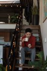 Чоловік має каву під час використання мобільного телефону на сходах вдома — стокове фото