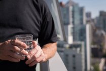Средняя часть человека держит стакан воды на балконе — стоковое фото