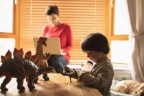 Boy playing toys while mother using laptop at home — Stock Photo