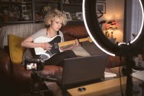 Женщина-блоггер играет на гитаре в гостиной дома — стоковое фото