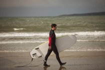 Surfer with surfboard walking on the beach on a sunny day — Stock Photo