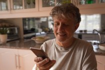 Senior benutzte Handy zu Hause in der Küche — Stockfoto
