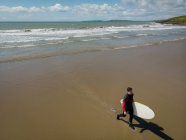 Vue grand angle de Surfeur avec planche de surf marchant sur la plage — Photo de stock