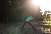 Atleta feminina realizando alongamento pela manhã na floresta — Fotografia de Stock