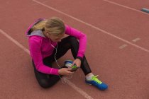 Female athlete listening music on mobile phone at running track — Stock Photo