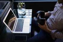 Uomo d'affari in possesso di cuffia realtà virtuale mentre si lavora sul computer portatile in ufficio — Foto stock