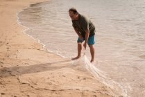 Зрелый рыбак держит рыболовные сети на пляже — стоковое фото