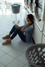 Mulher sorridente usando seu telefone enquanto espera na lavanderia — Fotografia de Stock