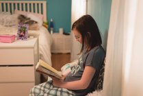 Fille lisant un livre dans la chambre à coucher à la maison — Photo de stock
