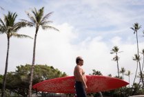 Hombre surfista sosteniendo tabla de surf en la playa - foto de stock