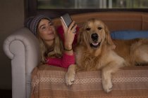 Дівчина з собакою використовує мобільний телефон у вітальні вдома — стокове фото