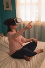 Fille en utilisant un casque de réalité virtuelle dans la chambre à coucher à la maison — Photo de stock