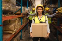 Portrait of female Staff holding cardboard box in warehouse — Stock Photo