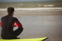 Vista traseira do surfista sentado na prancha de surf na praia — Fotografia de Stock