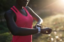 Середина жіночого спортсмена перевіряє свій смарт-годинник у лісі — стокове фото