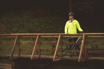 Giovane motociclista in piedi su un ponte di legno nel bosco — Foto stock