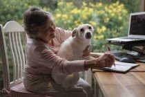 Seniorin sitzt mit Hund beim Tagebuchschreiben zu Hause — Stockfoto