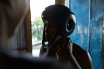 Trainer assisting male boxer to wear headgear in fitness studio — Stock Photo