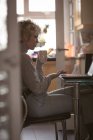 Jovem mulher usando laptop enquanto toma café em casa — Fotografia de Stock