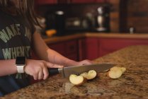 Chica de corte de manzana en la cocina en casa - foto de stock