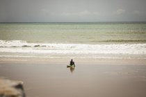Серфер, сидячи на дошці на пляжі і дивлячись на море в сонячний день — стокове фото